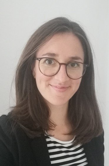 Porträt einer lächelnden Frau mit Brille und langen braunen Haaren.