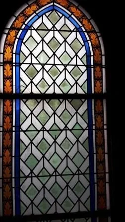 Ein Buntglasfenster mit geometrischen Mustern und einem Blattrand.