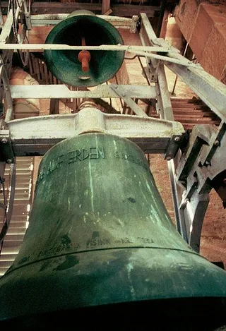 Eine Nahaufnahme von zwei großen, grünen Kirchenglocken in einem Glockenturm.