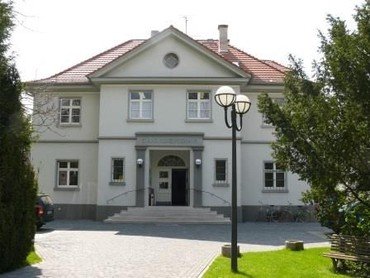 Das weiße, zweistöckige Gebäude des Gemeindezentrums mit Giebeldach.