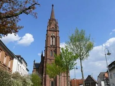 Die Backsteinkirche in Langen mit Kirchturm und Uhr vor blauem Himmel.
