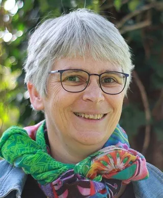 Porträt einer lächelnden Frau mit Brille und kurzen grauen Haaren.