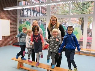 Eine Gruppe lächelnder Kinder und zwei Erwachsene auf einem Schwebebalken.