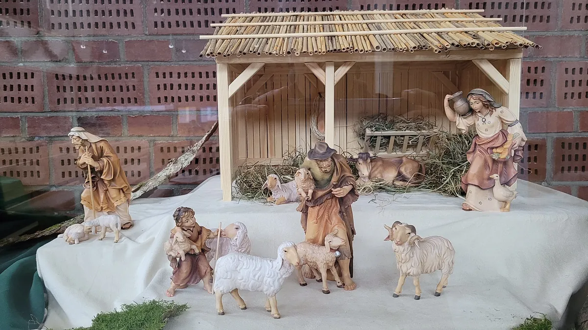Eine Krippenszene mit Hirtenfiguren, Schafen und dem Stall.