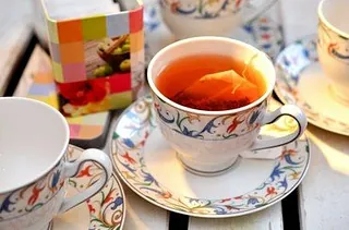 Eine Tasse Tee mit Teebeutel, einer verzierten Teetasse und einer bunten Dose.