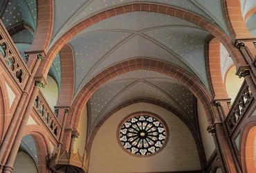 Innenansicht einer Kirche mit einem Sternengewölbe und einem Rosettenfenster.