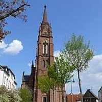 Die Backsteinkirche in Langen mit Kirchturm und Uhr vor blauem Himmel.