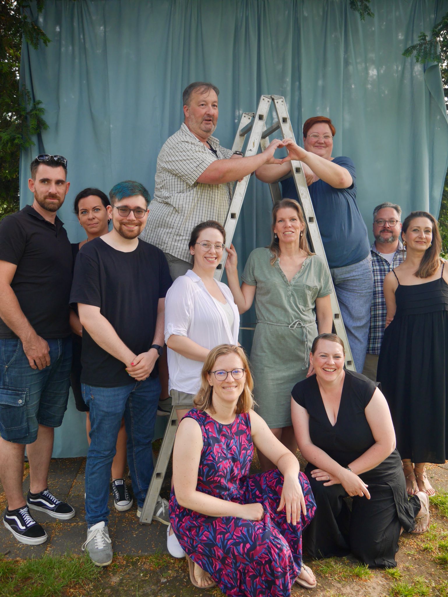 Eine lächelnde Gruppe von zehn Erwachsenen posiert vor einem blauen Vorhang.