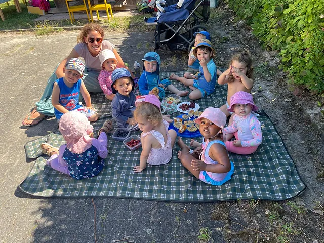 Eine Gruppe von Kleinkindern und eine Frau bei einem Picknick im Freien.