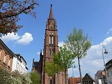Die Backsteinkirche in Langen mit Kirchturm und Uhr vor blauem Himmel.