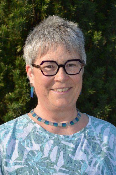 Porträt einer lächelnden Frau mit Brille und kurzen grauen Haaren.