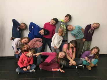Eine Gruppe von lachenden Kindern, die an einer weißen Wand posieren und sich anlehnen.