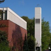Ein modernes Kirchengebäude mit roter Backsteinmauer und einem weißen Glockenturm.